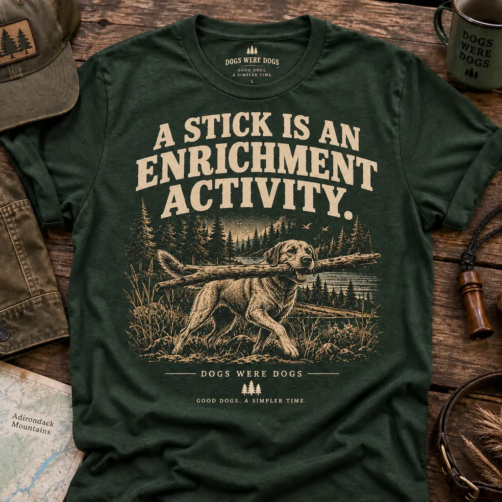 A Stick Is an Enrichment Activity t-shirt in heather forest green, printed with an engraved dog trotting in profile carrying a branch far too large for it, laid flat on weathered wood.